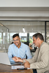 Wall Mural - Two busy happy professional business people men executive team, male partners working using laptop, manager consulting worker talking managing online finance data in office sitting at desk. Vertical.