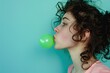 Young woman blowing up green bubble with chewing gum on green background