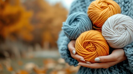 Wall Mural - a woman holding three skeins of yarn in her hands in front of a tree with yellow and blue leaves.