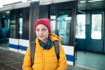 An 11-year-old schoolboy, student, boy in a jacket with a backpack exits the train carriage