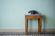 vintage black telephone covered in dust reststing on a small wooden table against a plain wall.