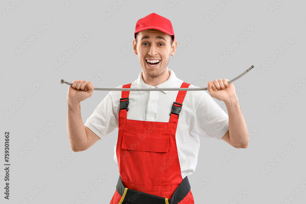 Male plumber with flexible hose on grey background
