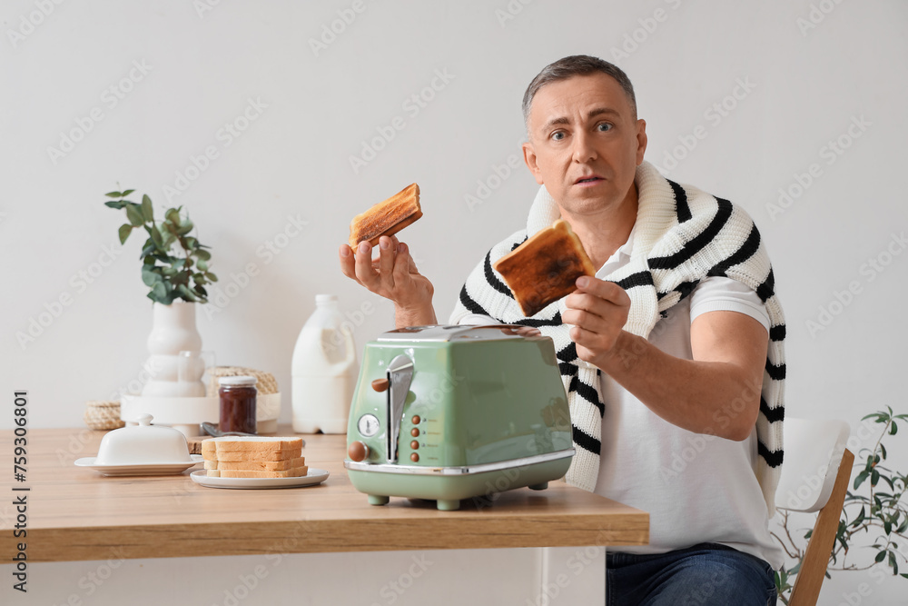 Confused middle-aged man with burnt toasts in kitchen