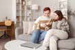 © Pixel-Shot - Young couple using mobile phone on sofa in living room