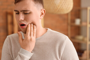 Wall Mural - Young man suffering from toothache at home, closeup