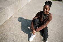 Portrait Of Black Young Woman In The City, Sitting Down On Concrete