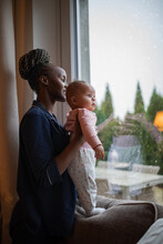 African American Mother Looking Out Of Window With Baby