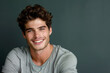 A man with curly hair is smiling and wearing a grey shirt