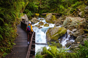 hiker girl admiring a rushing river with waterfalls in fiordland national park, new zealand south island, hiking trail to lake marian