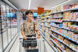 © Alvaro Lavin/Stocksy - Woman smiling while pushing shopping cart in grocery market aisle.