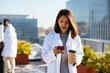 © BONNINSTUDIO/Stocksy - Doctor with coffee to go using smartphone
