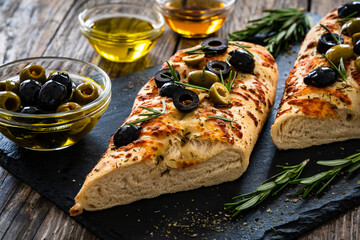 Wall Mural - Focaccia alle olive - baked sandwich with green and black olives and rosemary on wooden background
