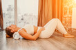 Adult athletic woman, in white bodysuit, performing fascia exercises on the floor - caucasian woman using a massage foam roller - a tool to relieve tension in the back and relieve muscle pain - the