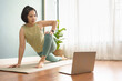 Healthy Young Asian Japanese sporty woman practicing yoga lesson on yoga mat in online class on laptop at home.