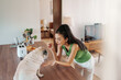 Attentive Asian woman in a vibrant green tank engaging with her pug dog at a modern kitchen table, embodying a cozy, nurturing home environment.