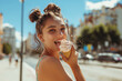 © J S - Teenage girl or young woman licking ice cream on hot summer street, tongue visible, copy space on blurred city background