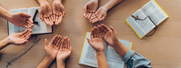 Wall Mural - Cropped image of diversity people hand praying together at wooden church on bible book. Group of believer hold hand together faithfully. Concept of hope, religion, faith, god blessing. Burgeoning.