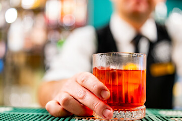 Wall Mural - bartender serving a red cocktail at a bar. The focus is on the glass and the bartender’s hand. The drink is bright red and served in a short, clear, textured glass