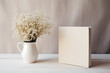White book mockup with gypsophila in a vase on a beige table