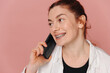 Modern happy woman smiling widely with braces and talking on smartphone on pink background