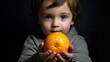 Close-up of a young child holding an orange, with a focused expression on a dark background