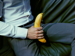 A  man in a suit holding a banana between his legs, symbolizing his penis in an erect state.