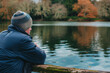 Individual in winter attire enjoys a tranquil moment by a picturesque lake surrounded by fall foliage