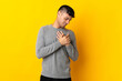 Young Colombian man isolated on yellow background having a pain in the heart