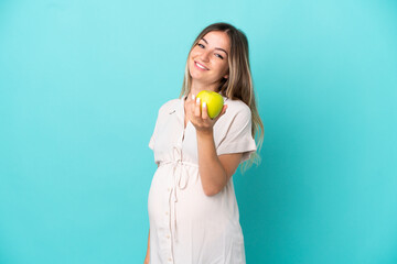 Wall Mural - Young Romanian woman isolated on blue background pregnant and holding an apple