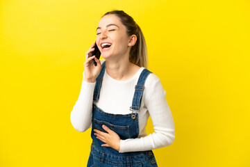 Wall Mural - Young woman using mobile phone over isolated yellow background smiling a lot