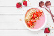 Healthy strawberry and banana smoothie bowl with granola. Overhead view table scene on a white wood background. Copy space.