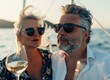 Happy middle-aged man and woman couple sitting and drinking wine on a yacht at sea, enjoying their summer vacation time together.