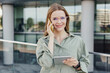 © muse studio - Smiling businesswoman multitasking with phone and tablet outdoors.