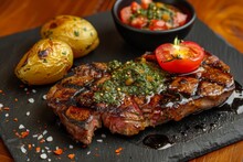 A Cooked Steak Sits On A Plate With A Side Of Roasted Potatoes And A Fresh Tomato, Ready To Be Enjoyed.