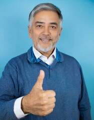 Senior man standing over isolated blue background doing happy thumbs up gesture with hand