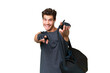 © luismolinero - Young sport caucasian man with sport bag over over isolated background points finger at you while smiling