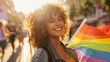 Happy curly haired female student celebrating gay rights with a rainbow flag at pride parade. Pride festival march during golden hour