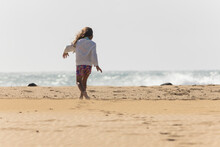 Anonymous young girl enjoys her freedom, running towards the sea spray on a sunlit beach, encapsulating the essence of carefree childhood