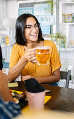 Wall Mural - Happy young woman holding beer enjoying brunch with friends at bar. Food and drink concept.