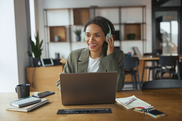 A woman wears headphones while using a laptop on a table in nice modern coworking office