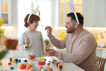 Sticker - Easter celebration. Father with his little son having fun while painting eggs at white marble table in kitchen