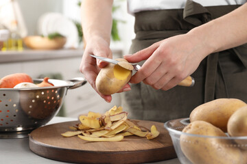 Woman peeling fresh potato with knife at light table indoors, closeup