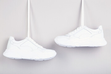 Wall Mural - Pair of hanging white shoes on grey background