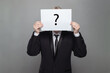 © millaf - Formal anonymous person hiding his head behind white paper with question mark against gray studio wall background