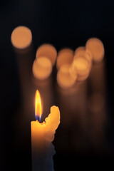 Close up of burning church candle with blurred lights against dark background