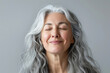 A gorgeous happy smiling senior woman with closed eyes and long grey hair over a grey background