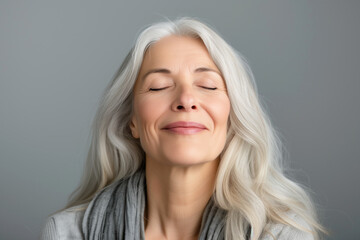 Wall Mural - A gorgeous happy smiling senior woman with closed eyes and long grey hair over a grey background