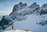 Fototapeta Na ścianę - Adventurous man hiker on top of a steep rocky cliff overlooking winter alpine like moutain landscape of High Tatras, Slovakia. Alpine mountain landscape covered with glaciers, snow and ice.