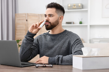 Canvas Print - Medical drops. Young man using nasal spray at table indoors