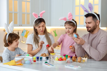 Wall Mural - Easter celebration. Happy family with bunny ears painting eggs at white marble table in kitchen